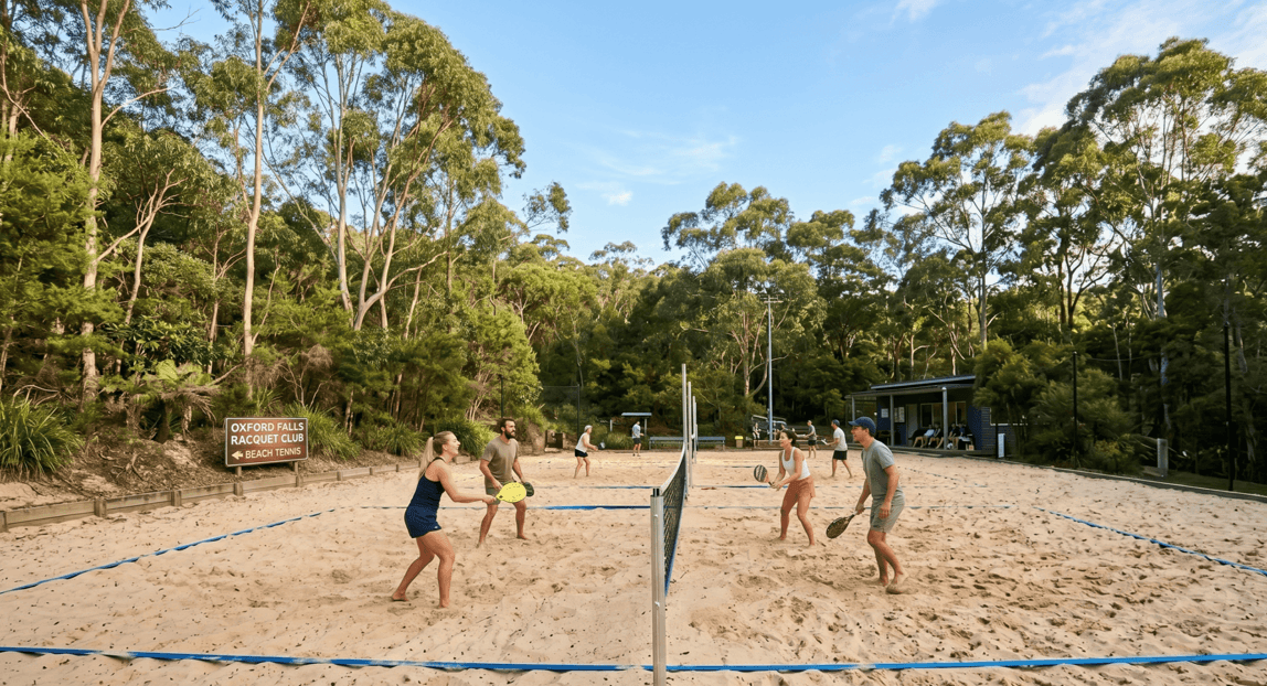 Wide-photo-of-the-beach-tennis-court-with-players-on-sand-showing-the-net-court-lines-and-surrounding-greenery-scaled